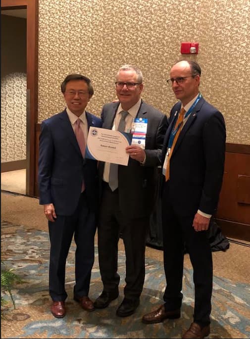 Dr. Brodell standing between two gentleman while holding up a certificate.